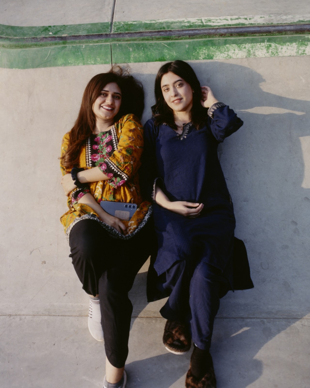 Two Pakistani skaters lay down next to each other in a skatepark.