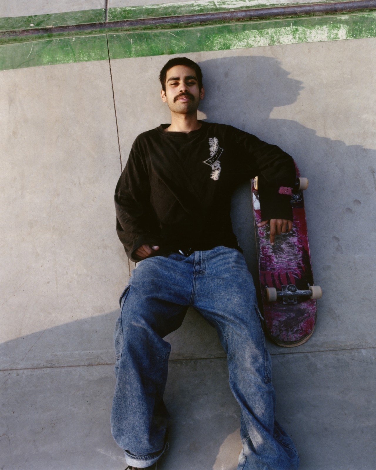A Pakistani skater lays down in a skatepark next to their skateboard.