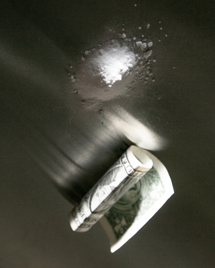 A rolled up dollar bill lays on a table next to a small pile of cocaine.