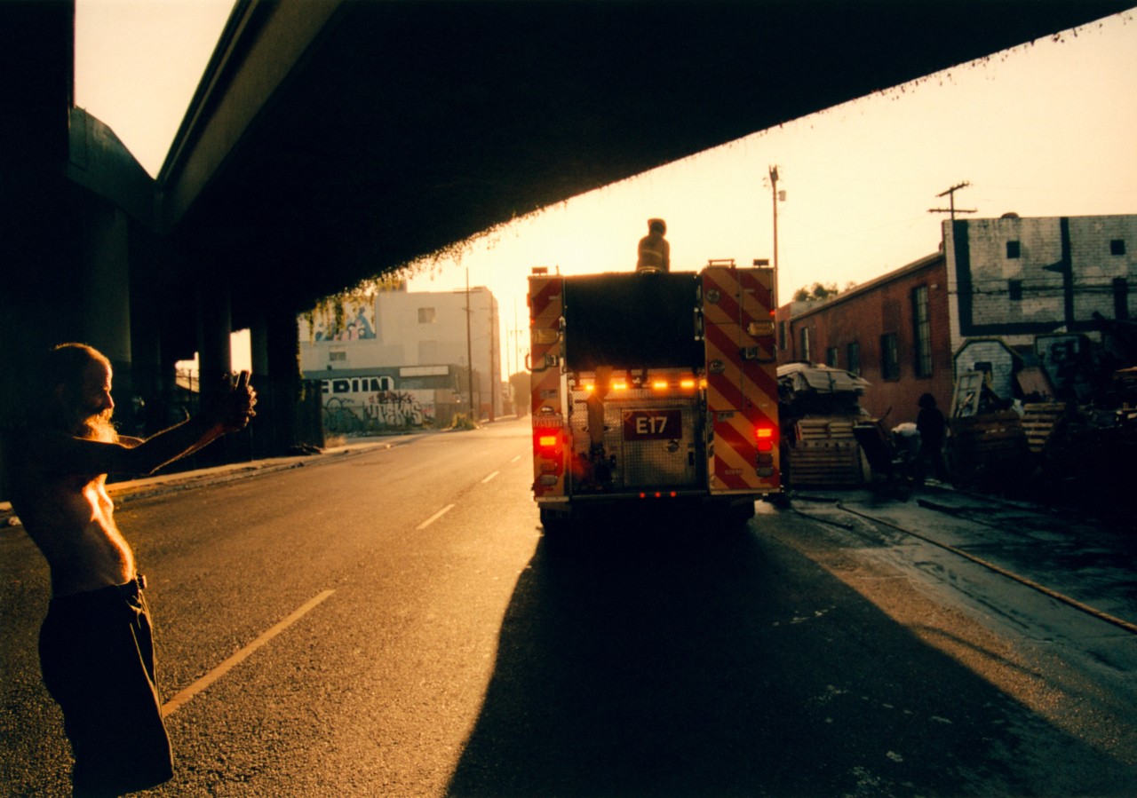A firetruck drives down the street under a freeway as the sun sets.