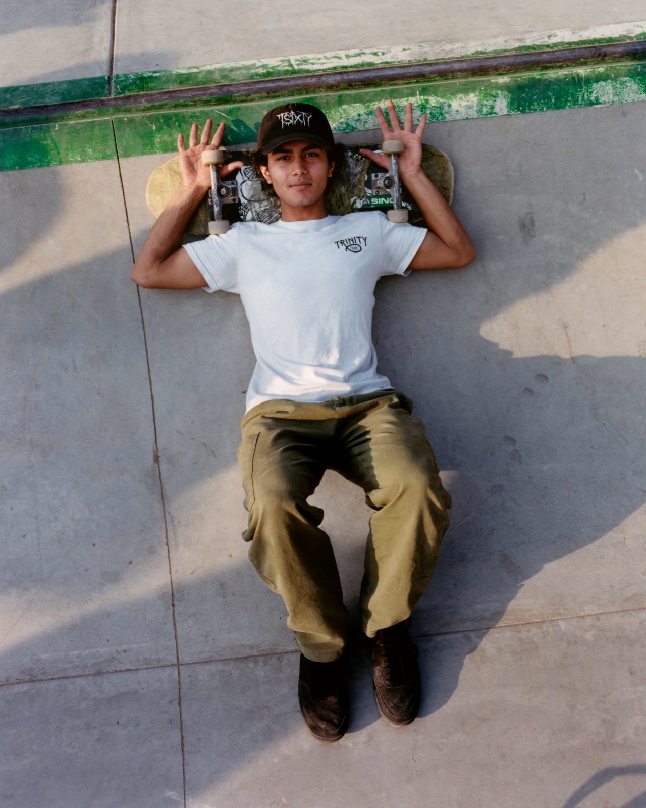 Young male skateboarder lying on ground with head on skateboard.