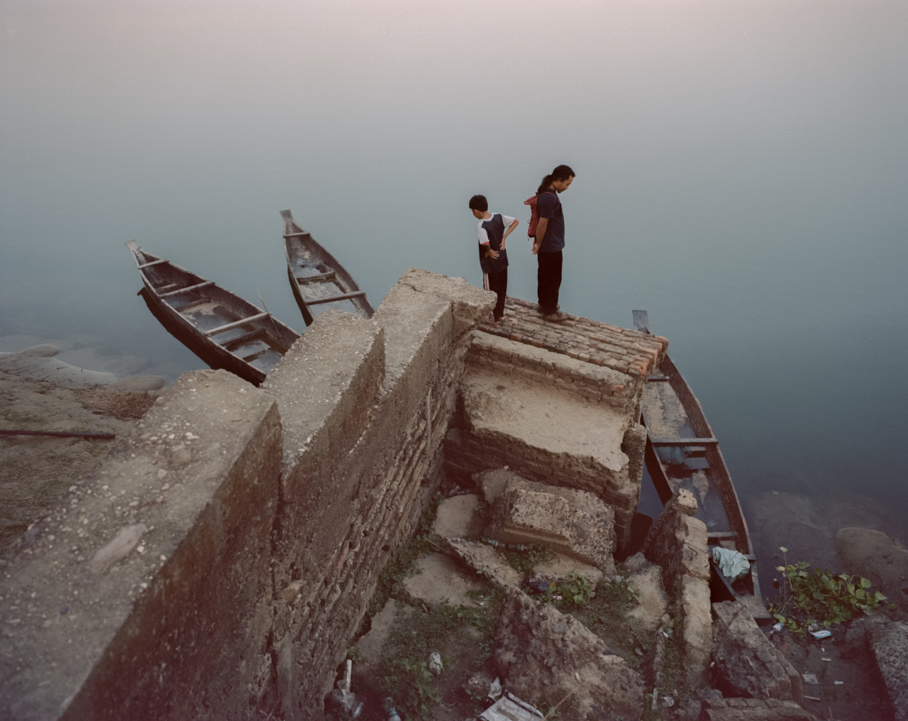 Two people stand on concrete above the river.