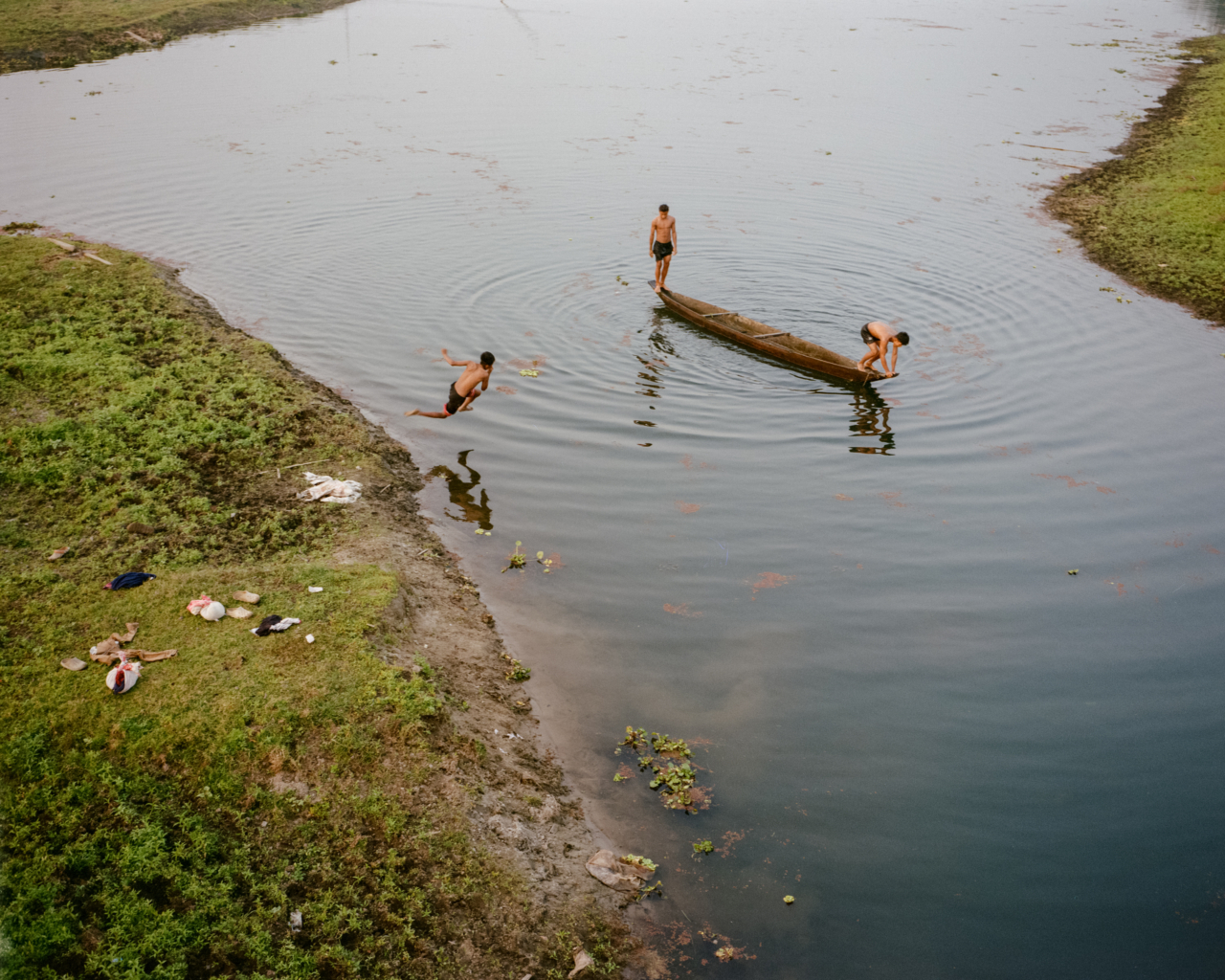 Three people on and near a canoe in the Brahmaputra river.