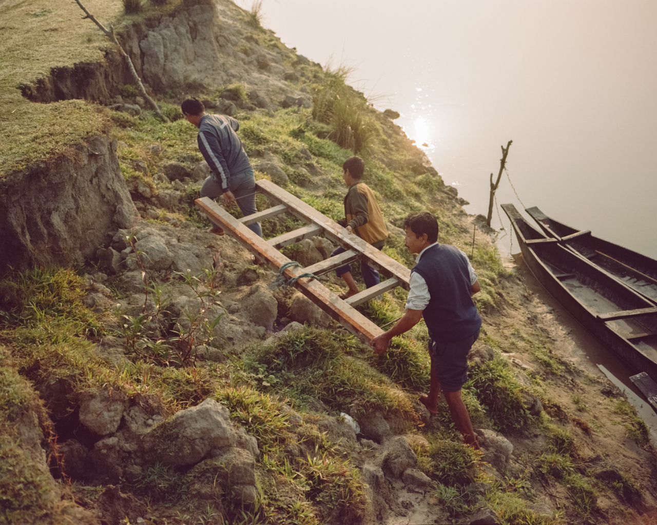 Three people carry a ladder up a hill.