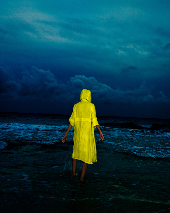 A person wearing a yellow raincoat stands in front of the ocean.
