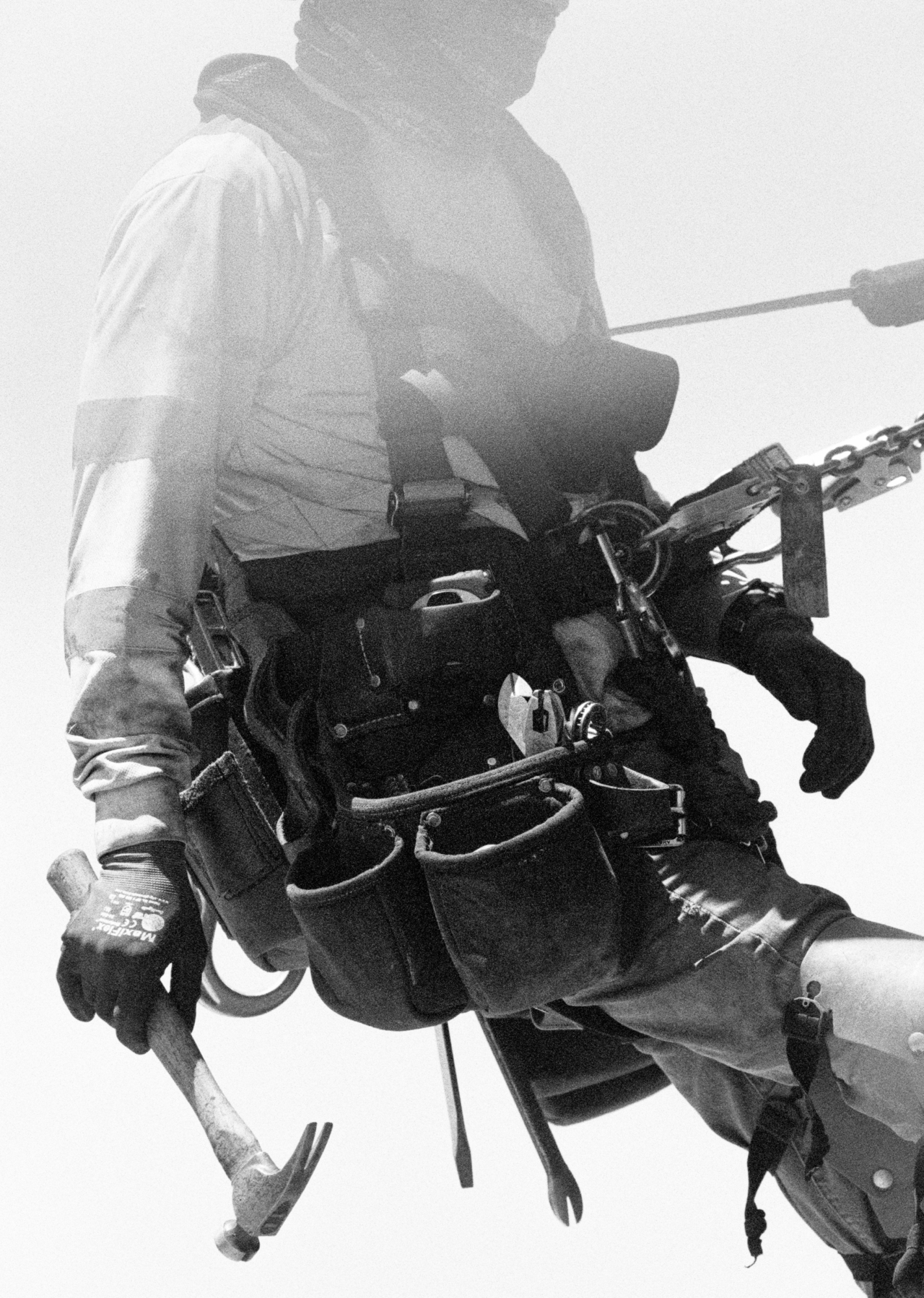 A worker carries a tool belt and holds a hammer.