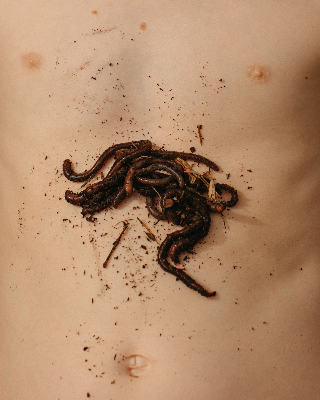 A handful of earthworms lays on a person's bare chest.