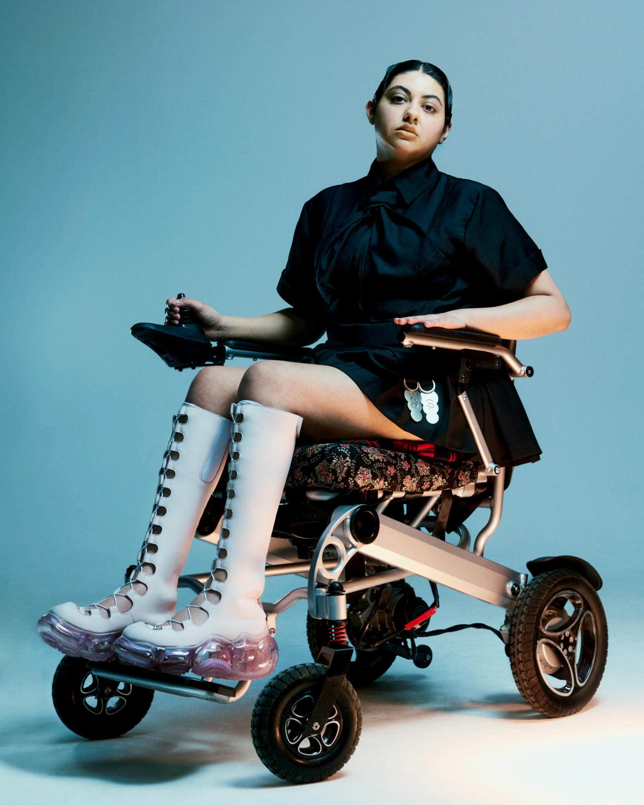 A person in a motorized wheelchair wears a black dress with white boots.