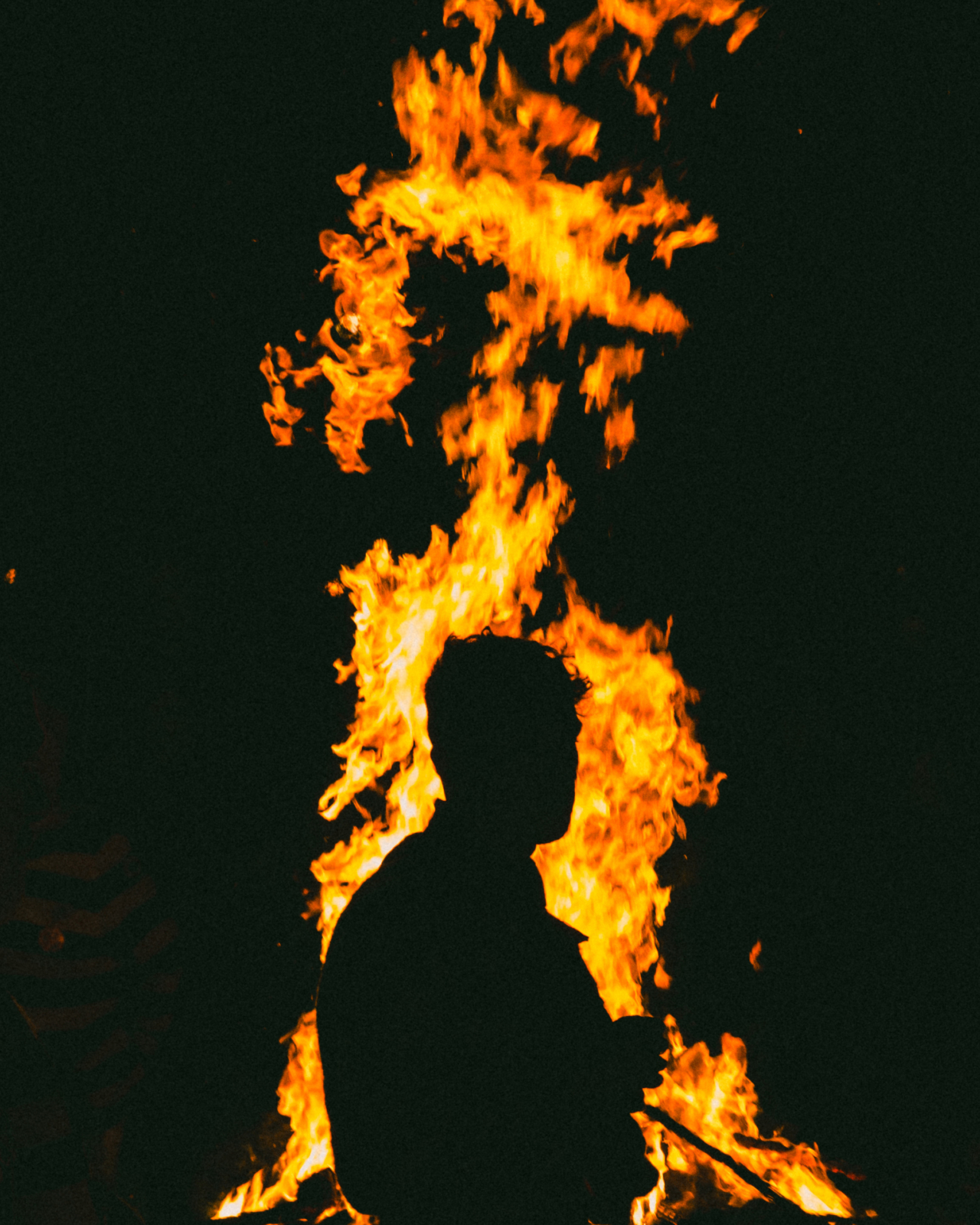 The shadow of a man stands in front of a large fire flame.