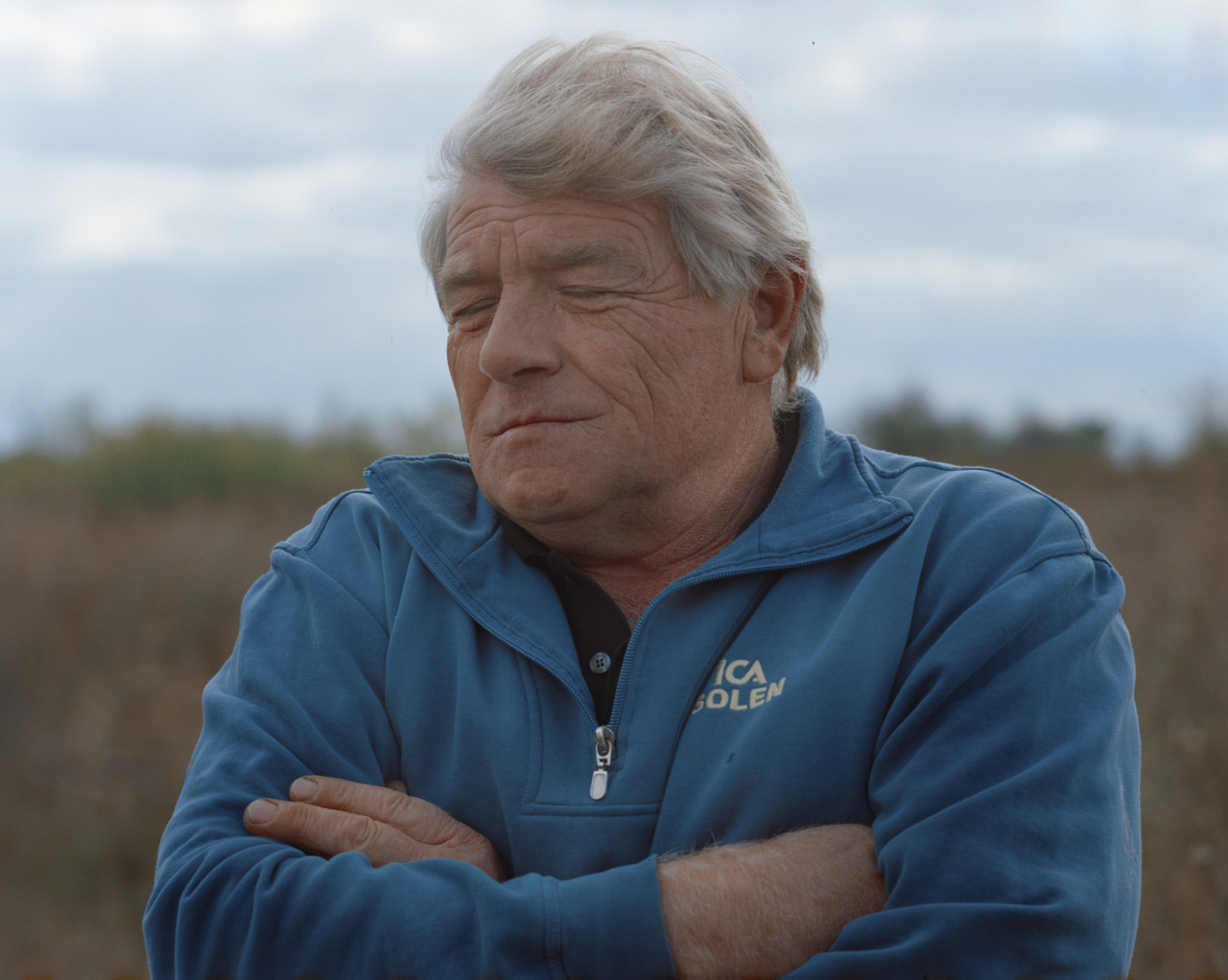 A man with gray folds his arms and closes his eyes.