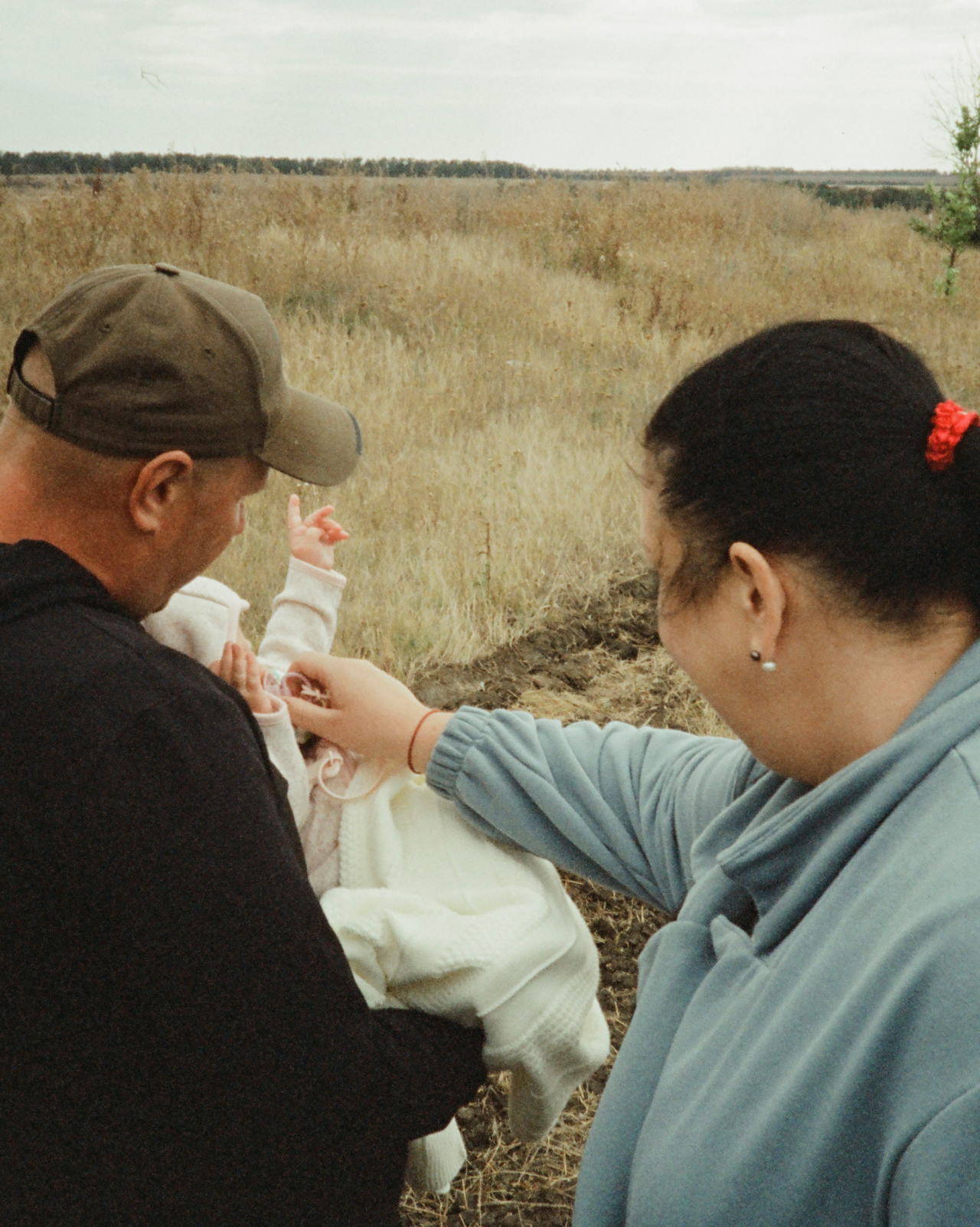 Two people hold a baby in a field.