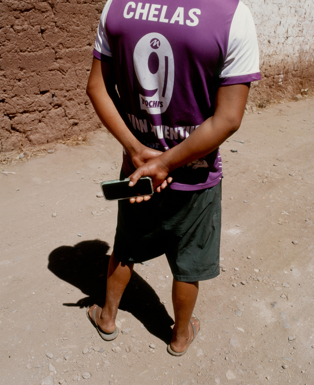 A man with a purple jersey holds his phone behind his back.