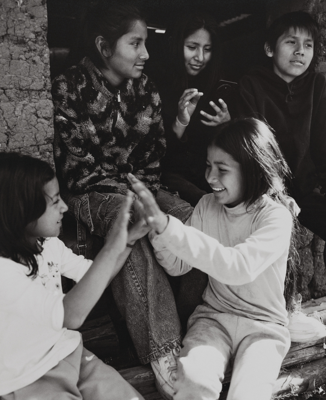 Children sit on a stoop and play hand clapping games.