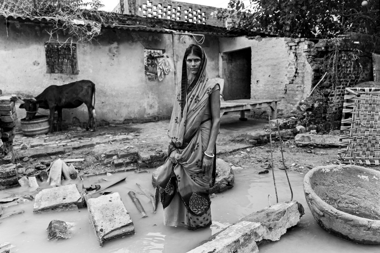 A woman shows the remains of her house, destroyed in the flood