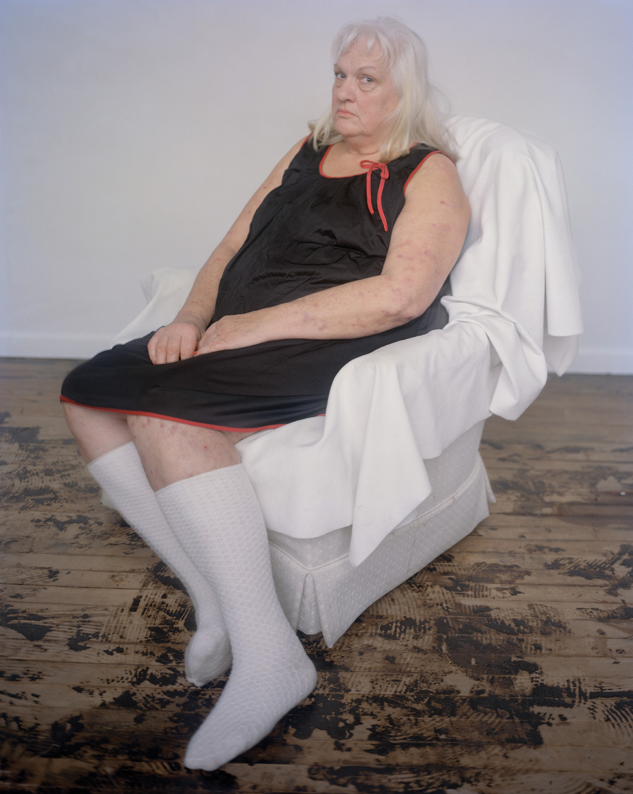 A mother dressed in a black dress and long white socks sits on a white chair.