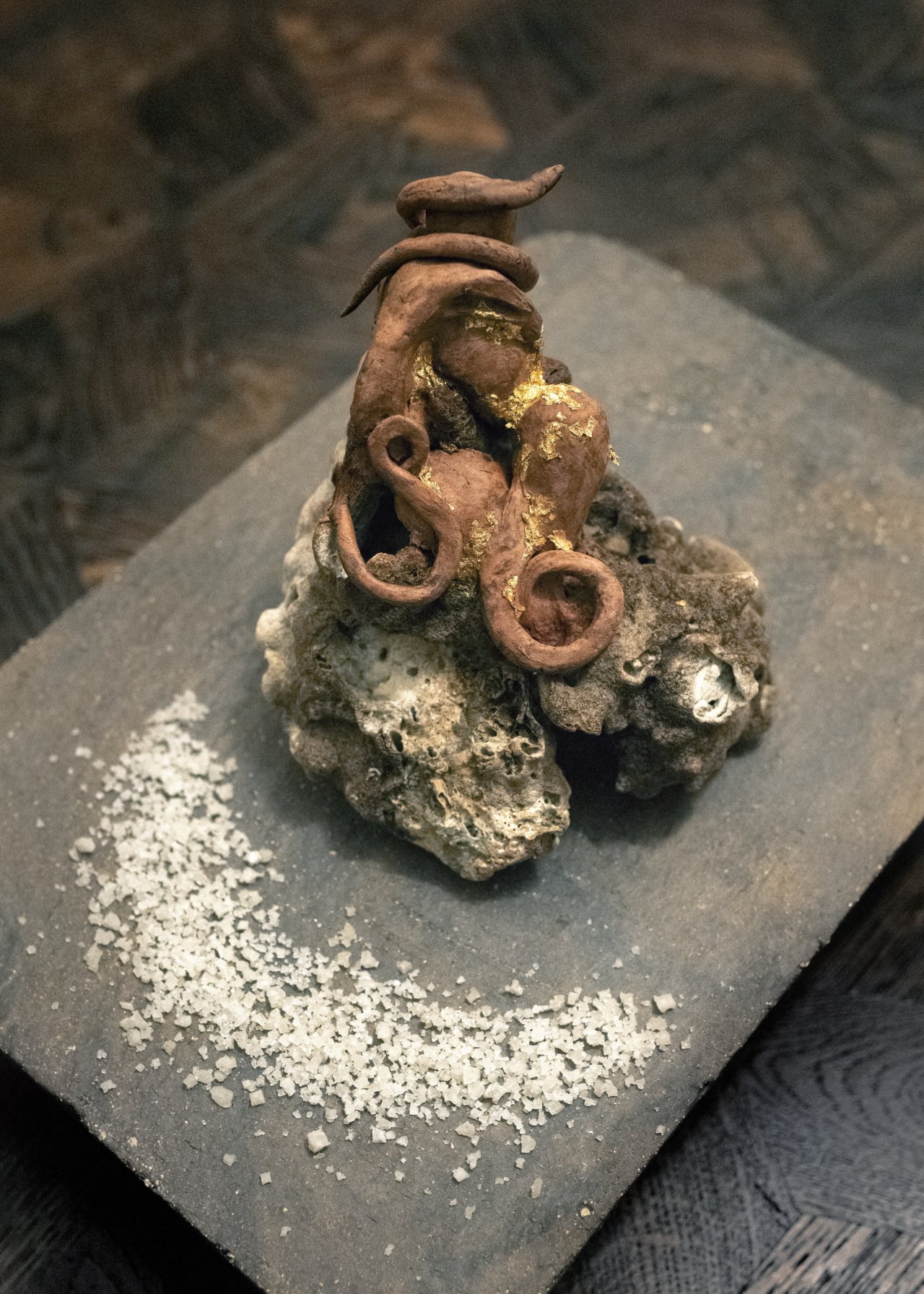 A clay sculpture sits on a wooden table.