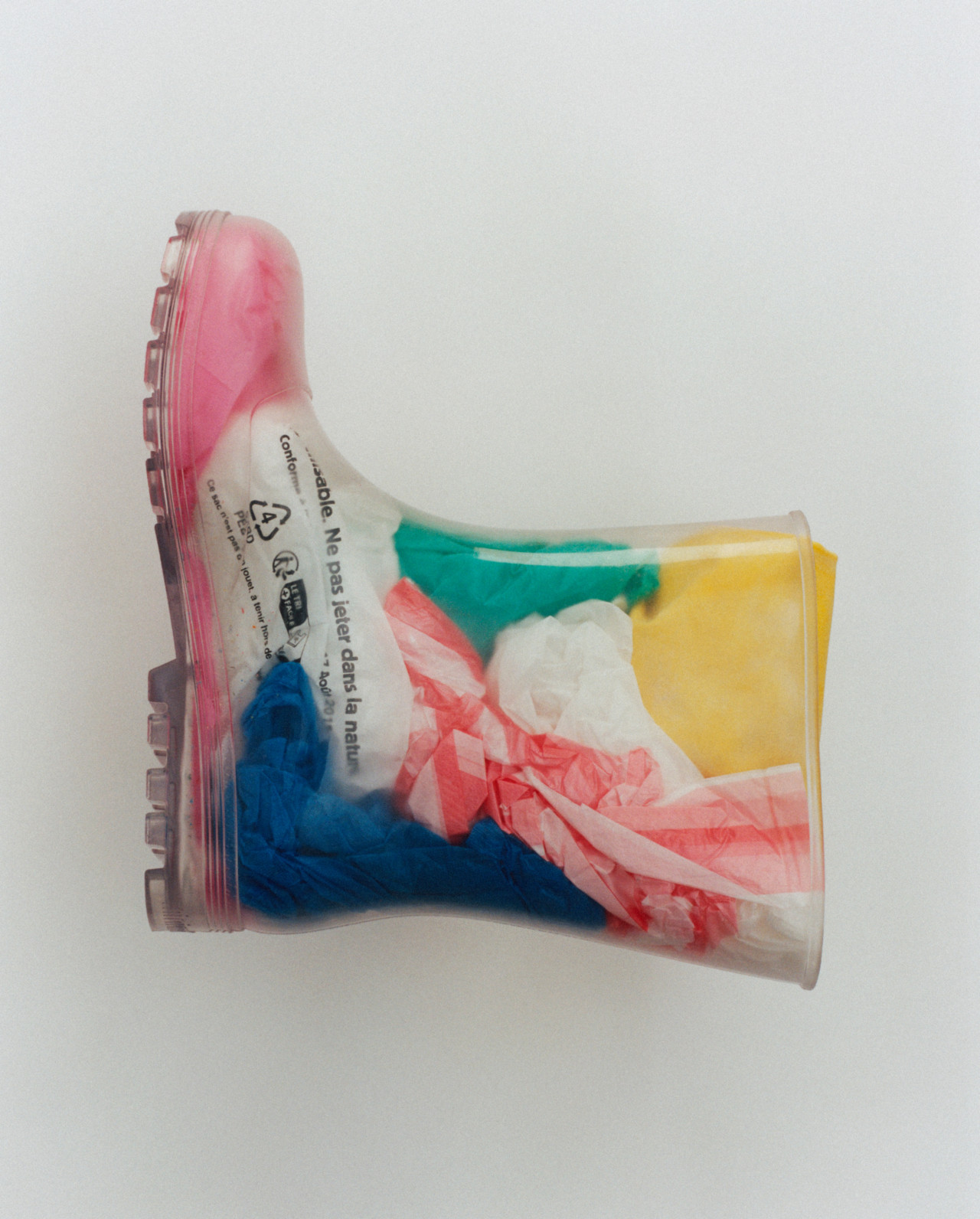 A transparent plastic boot filled with colorful plastic bags.