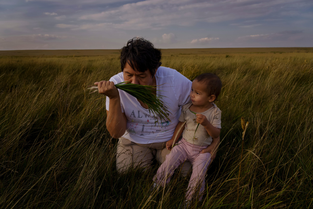 Holding her granddaughter close, a Blackfeet woman smells sweetgrass as the child watches intently, learning from a young age to recognize the plant by its sweet fragrance.