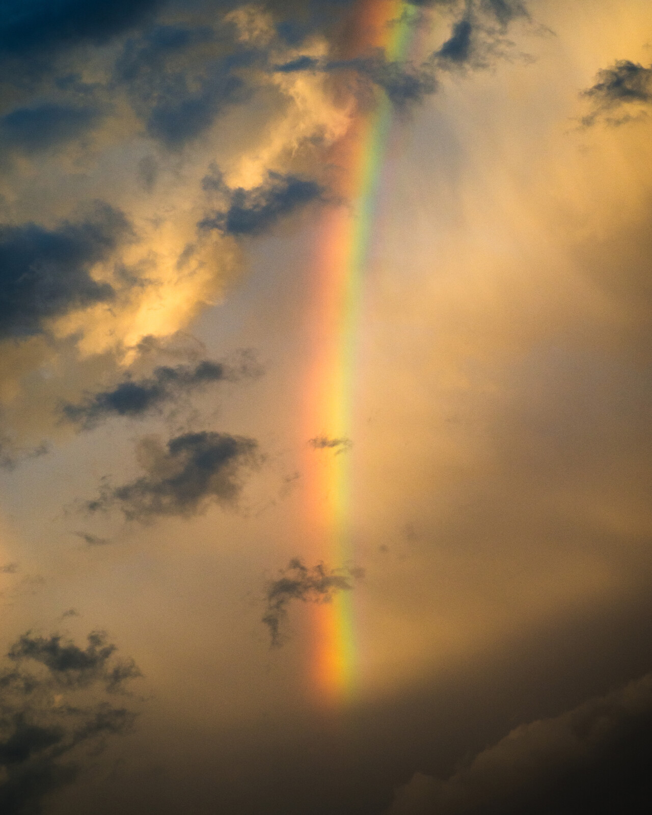 Photograph of a rainbow stretching across the sky with some clouds around it.
