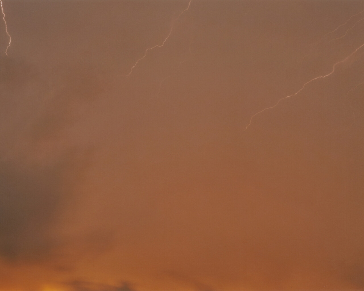 Photo showing thready streaks of lightning in a red, stormy sky