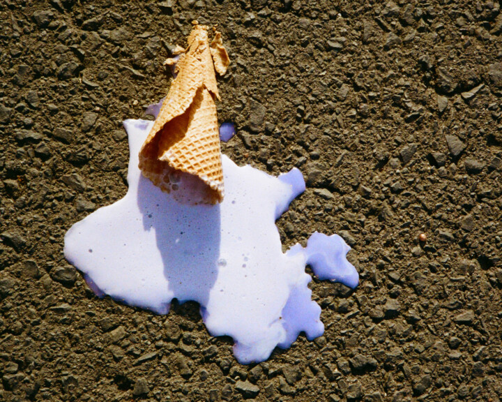 An ice cream cone and melted ice cream on the pavement.
